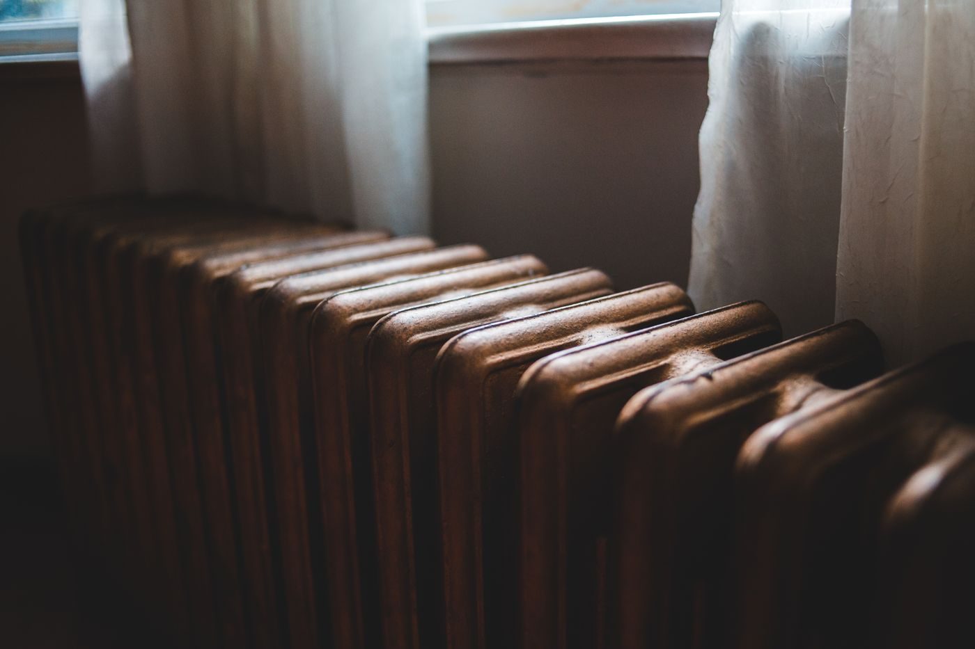 Cast iron radiator under a window with sheer curtains in soft daylight